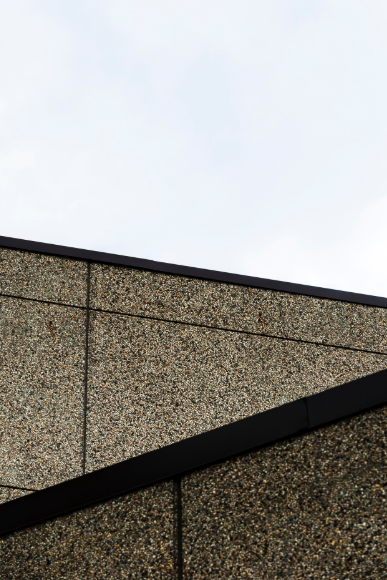 Close-up of a modern building facade featuring fine-grained natural stone cladding with clean joints and sharp architectural angles, highlighting professional exterior stone installation